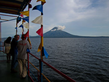 Rear view of men standing on railing by sea against sky