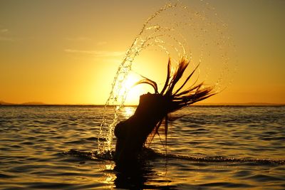 Silhouette woman splashing water from hair in sea against sky during sunset