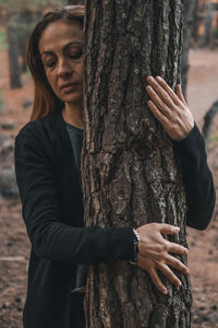 Young woman holding tree trunk