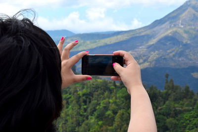 Midsection of woman photographing with mobile phone against sea