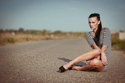 Portrait of young woman sitting on road against clear sky