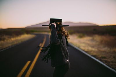 Woman in black hat and fringe dancing the street at sunset