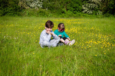 Cute redhead boy and girl sitting on the grass on a sunny day surrounded by yellow flowers
