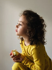 Side view of girl eating apple while sitting against wall at home