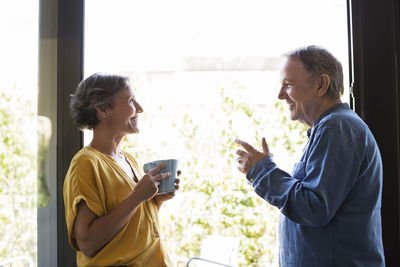 Side view of senior couple having coffee by window at home