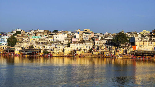 Buildings by river against clear blue sky.