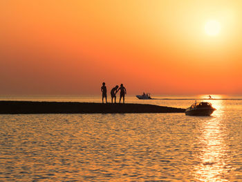 Scenic view of people by sea at sunset