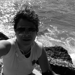 High angle portrait of woman wearing sunglasses while sitting on rocky shore