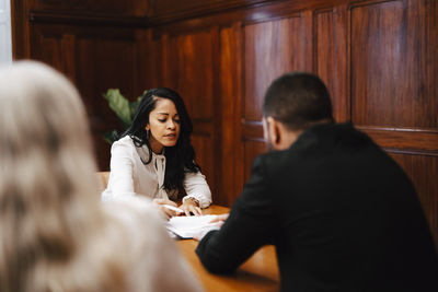Confident female financial advisor discussing over contract document with colleagues in board room