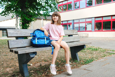 Back to school. a schoolgirl teenager sits on a bench next to a schoolbag in front of the school,