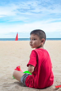 Portrait of boy sitting at beach against sky