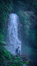 Man looking down while standing against waterfall