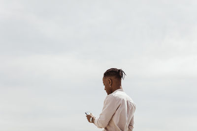 Young man using smart phone against clear sky on sunny day