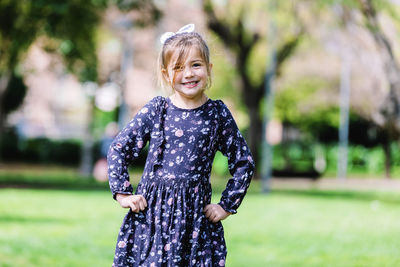 Portrait of cute smiling girl with arms akimbo standing in park