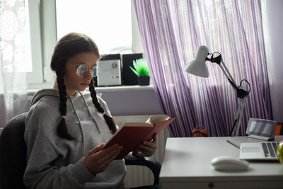 A teenager reads her school reading in her room at home.