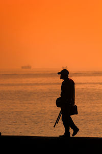 Silhouette man standing by sea against orange sky