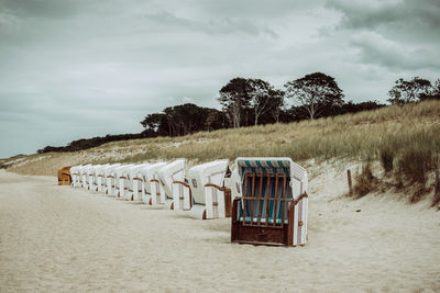 Hooded chairs on beach against cloudy sky