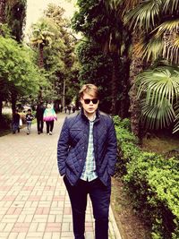 Portrait of young man standing on footpath by trees