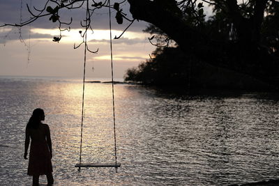 Rear view of woman standing by sea against sky during sunset