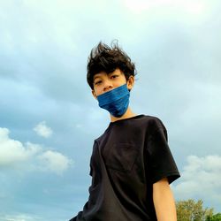 Low angle portrait of wearing mask standing against sky