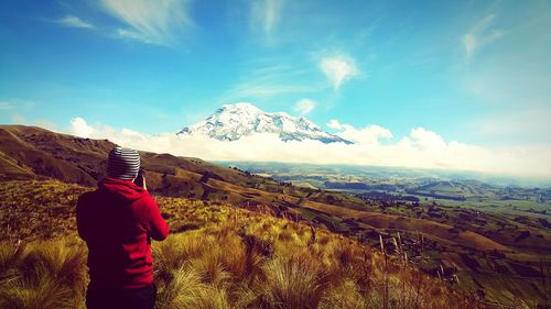 Rear view of mid adult man standing on mountain against sky during sunny day