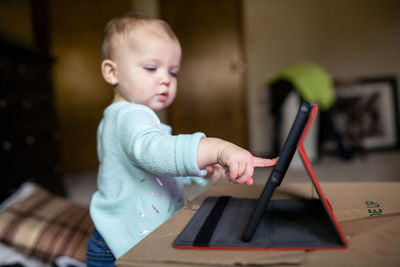 Cute baby girl using tablet computer while standing by box at home