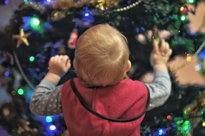 Rear view of baby girl standing by christmas tree at home