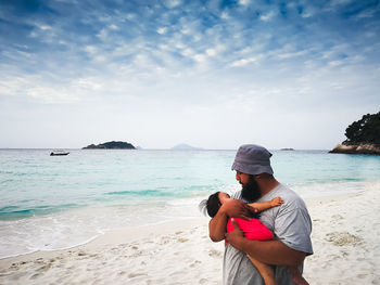 Father carrying daughter at beach against sky