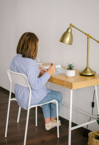 Rear view of woman sitting on table at home