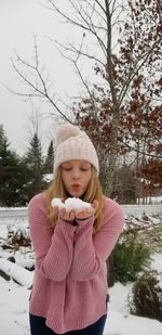 Teenage girl holding snow while standing against trees during winter