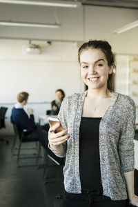 Portrait of smiling woman holding smart phone in classroom