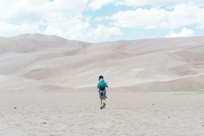 Rear view of boy on sand against sky