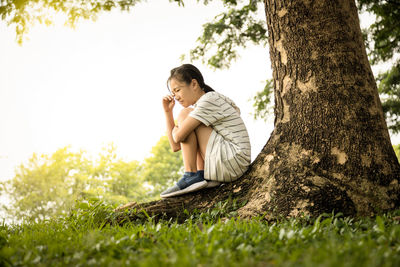 Young woman looking away while sitting on tree trunk in field