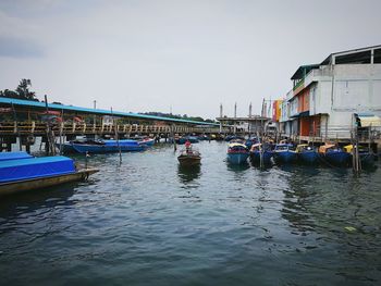 Boats moored at harbor against sky in city