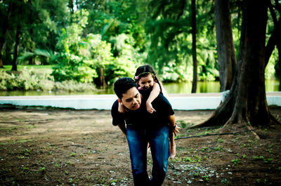 Father piggybacking daughter while walking on field against trees in forest