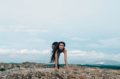 Young woman doing yoga on rock against sky