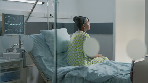 Young woman sitting on bed in hospital