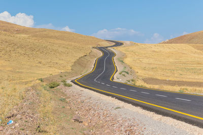 Country road leading towards mountains against sky