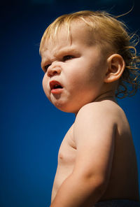 Side view of shirtless baby boy against blue sky