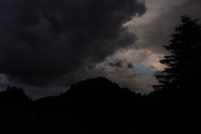 Low angle view of silhouette trees against storm clouds