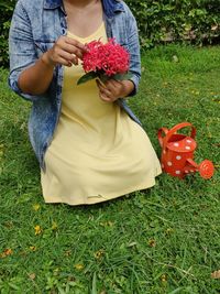 Midsection of woman holding red flower on field