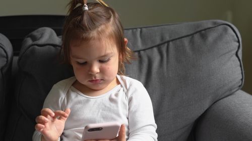 Full length of girl using mobile phone while sitting on sofa