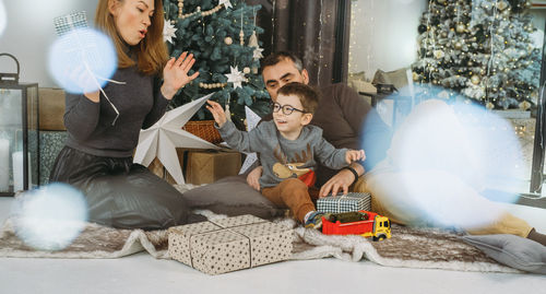 Family with child playing near christmas tree. child unpacking gifts, middle aged parents enjoy