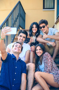 Man taking selfie with friends from mobile phone while sitting on steps
