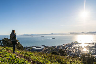 Rear view of woman standing on mountain against sea