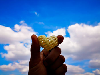 Close-up of hand holding ice cream against sky