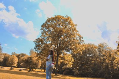 Teenage girl standing on field in forest against sky