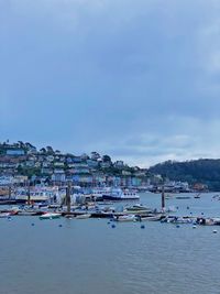 Sailboats moored in harbor by city against sky