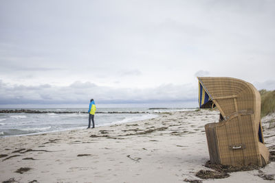 Hooded beach chair by man standing at sandy beach