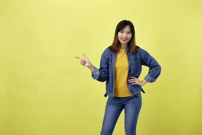 Portrait of smiling young woman standing against yellow background